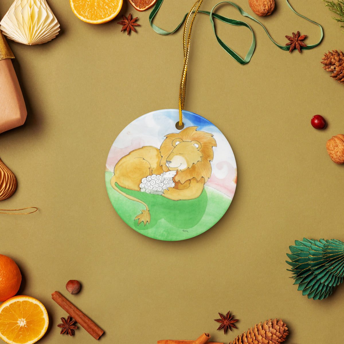 Lion and Lamb ceramic ornament on a gold string among holiday oranges and pinecones