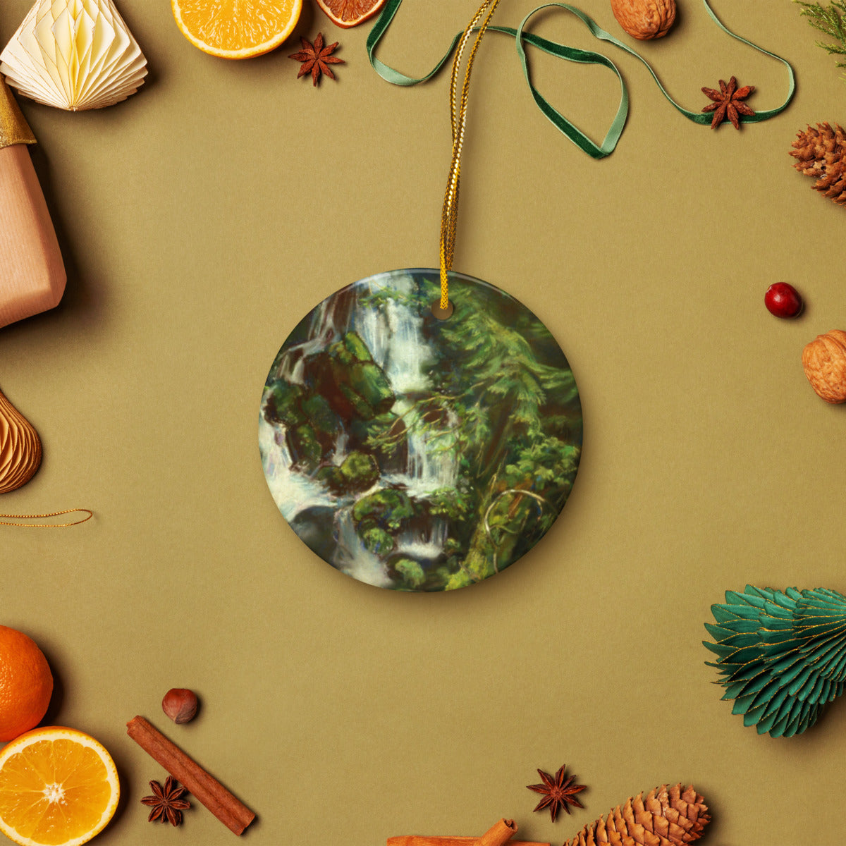 Woodland Waterfall ceramic ornament on a gold string among holiday oranges and pinecones